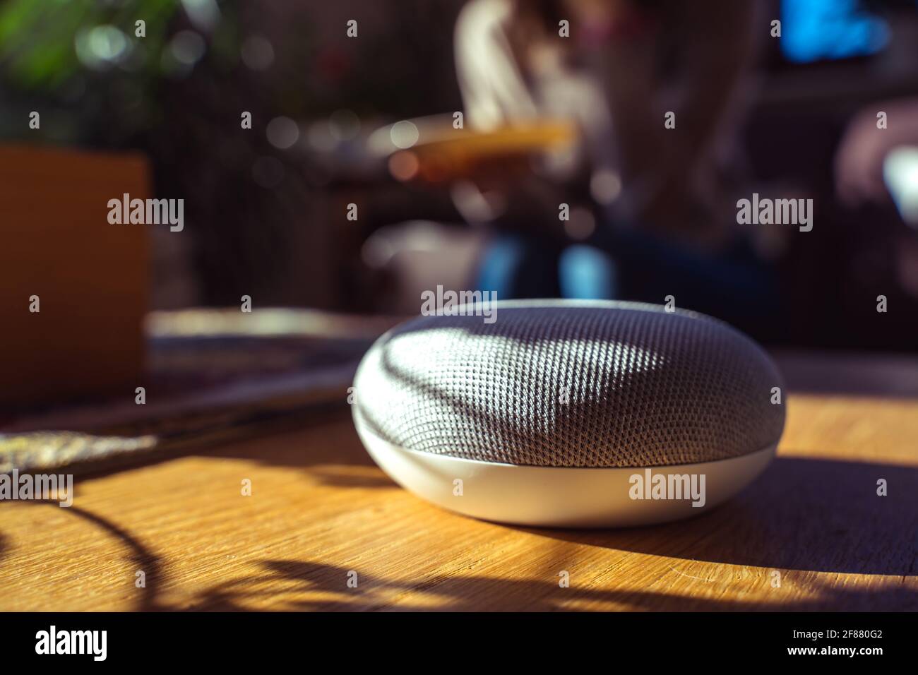 Sprachgesteuerter intelligenter Lautsprecher mit einer Frau im Hintergrund in einer Innenraumumgebung. Intelligentes AI-Lautsprecherkonzept Stockfoto