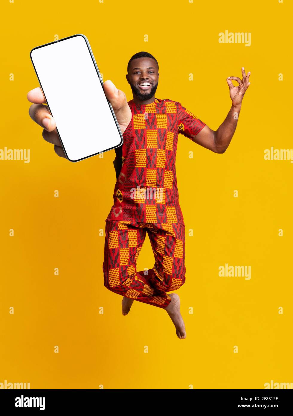 Tolle mobile Anwendung. Sorgloser afroamerikanischer Kerl in traditioneller Tracht, der mit dem Smartphone aufspringt, Mockup Stockfoto