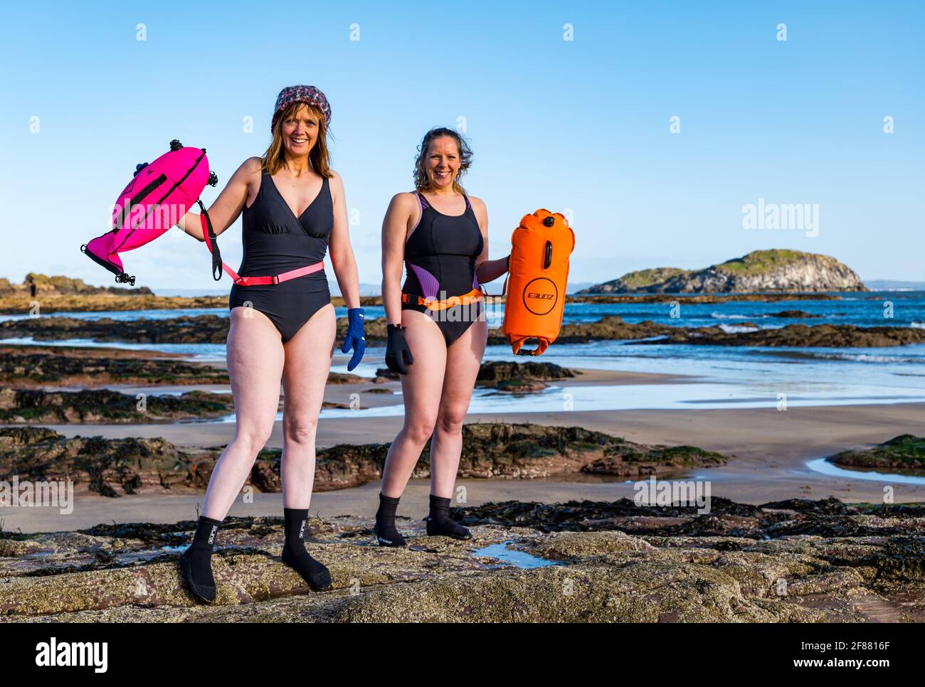 Zwei Frauen, die an einem sonnigen Tag im Freien oder im Freien schwimmen, in Badeanzügen mit Schwimmern am Strand, North Berwick, Firth of Forth, Schottland, Großbritannien Stockfoto