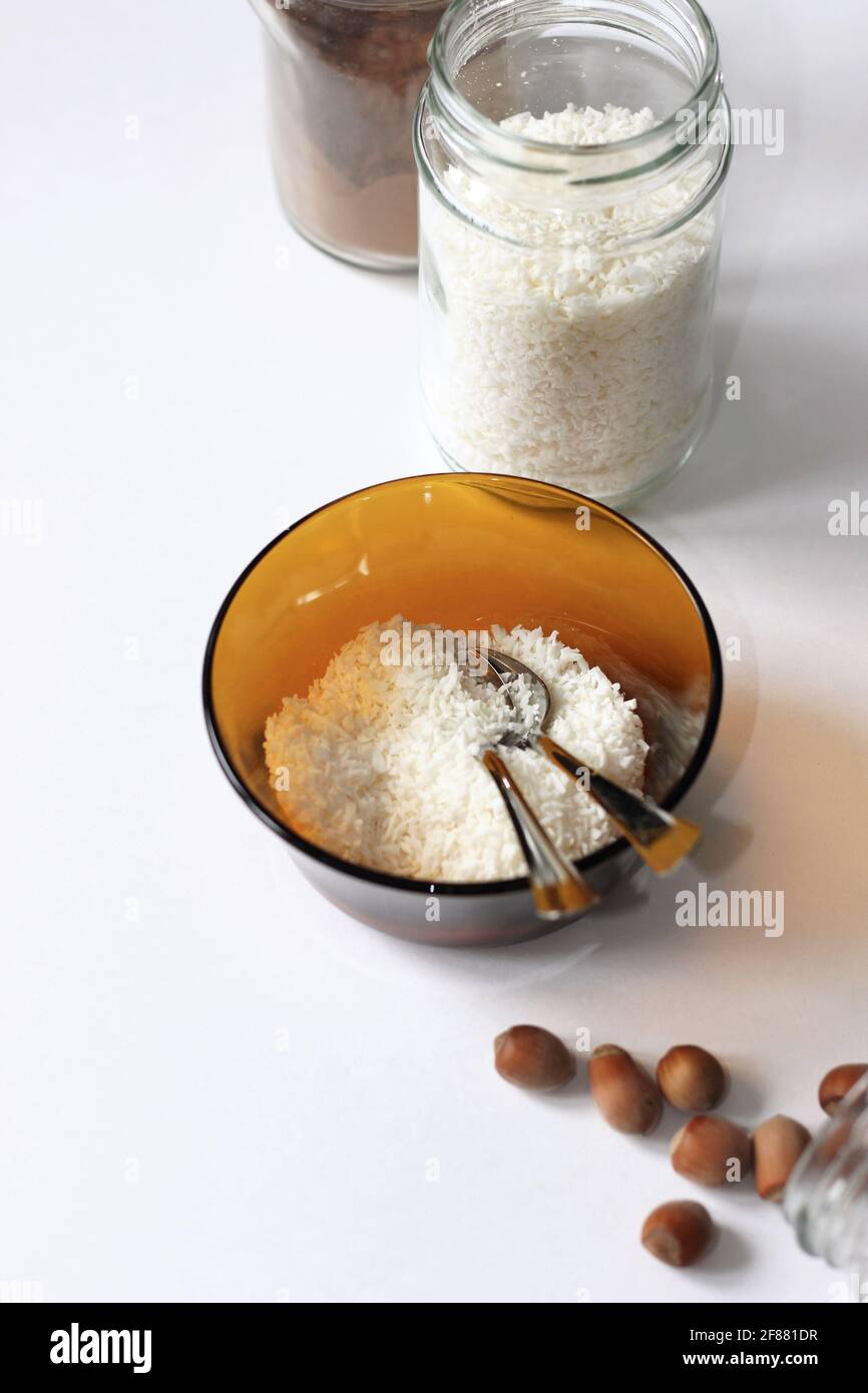 Gesunde Ernährung. Kokosflocken in Schale und Glasglas, Kanne Kakaopulver und Nüsse auf Weiß. Stockfoto