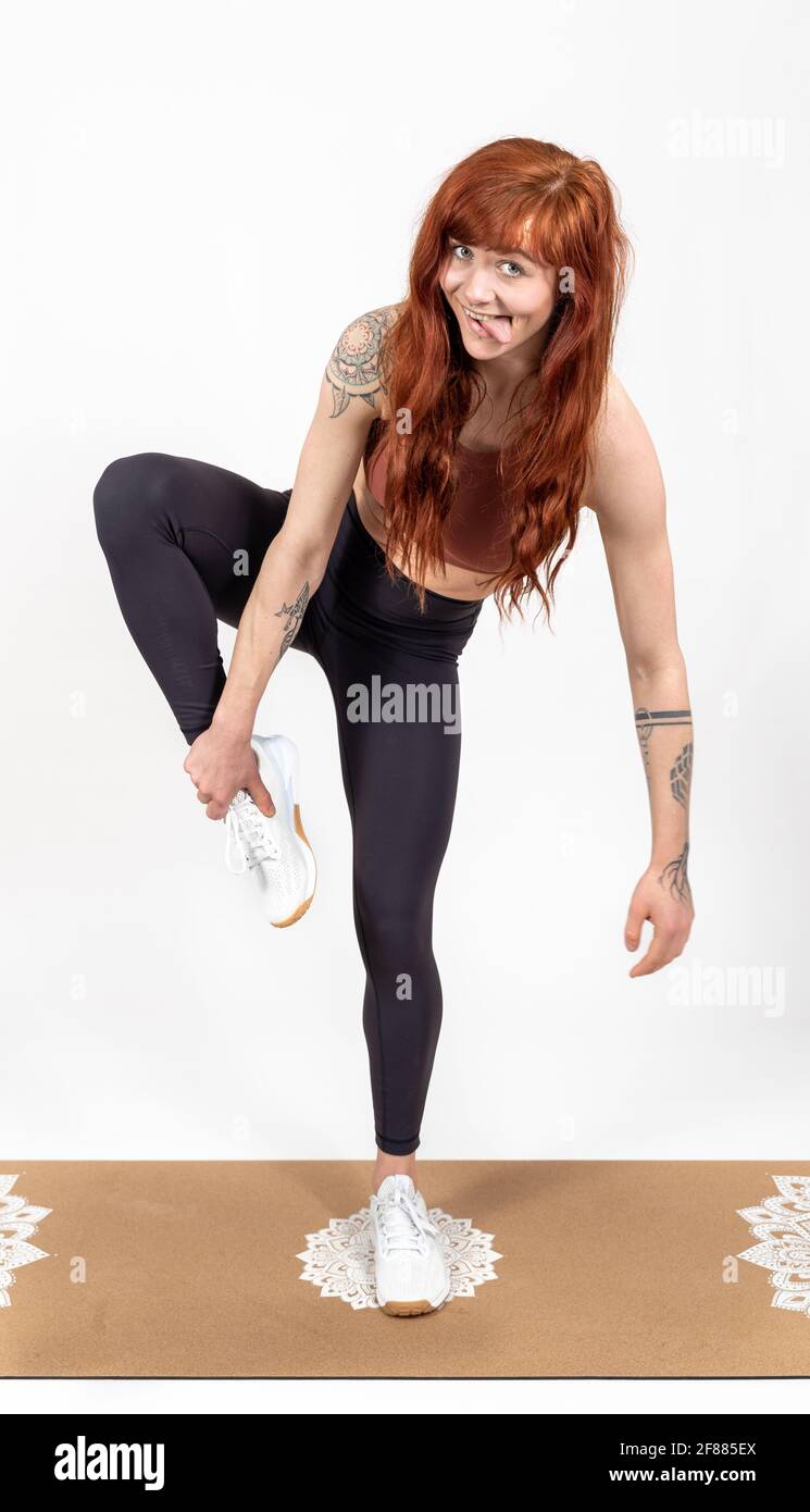 Frau mit roten Haaren auf weißem Hintergrund versucht, auszugleichen Während sportliche Ausbildung Stockfoto