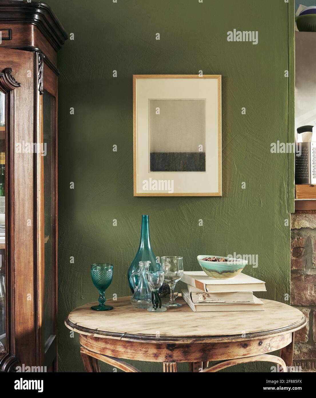 Modernes französisches Interieur. Alter Schrank, alter Tisch, Bücher und Gläser. Moderne Grafiken auf dunkelgrünem Hintergrund Stockfoto