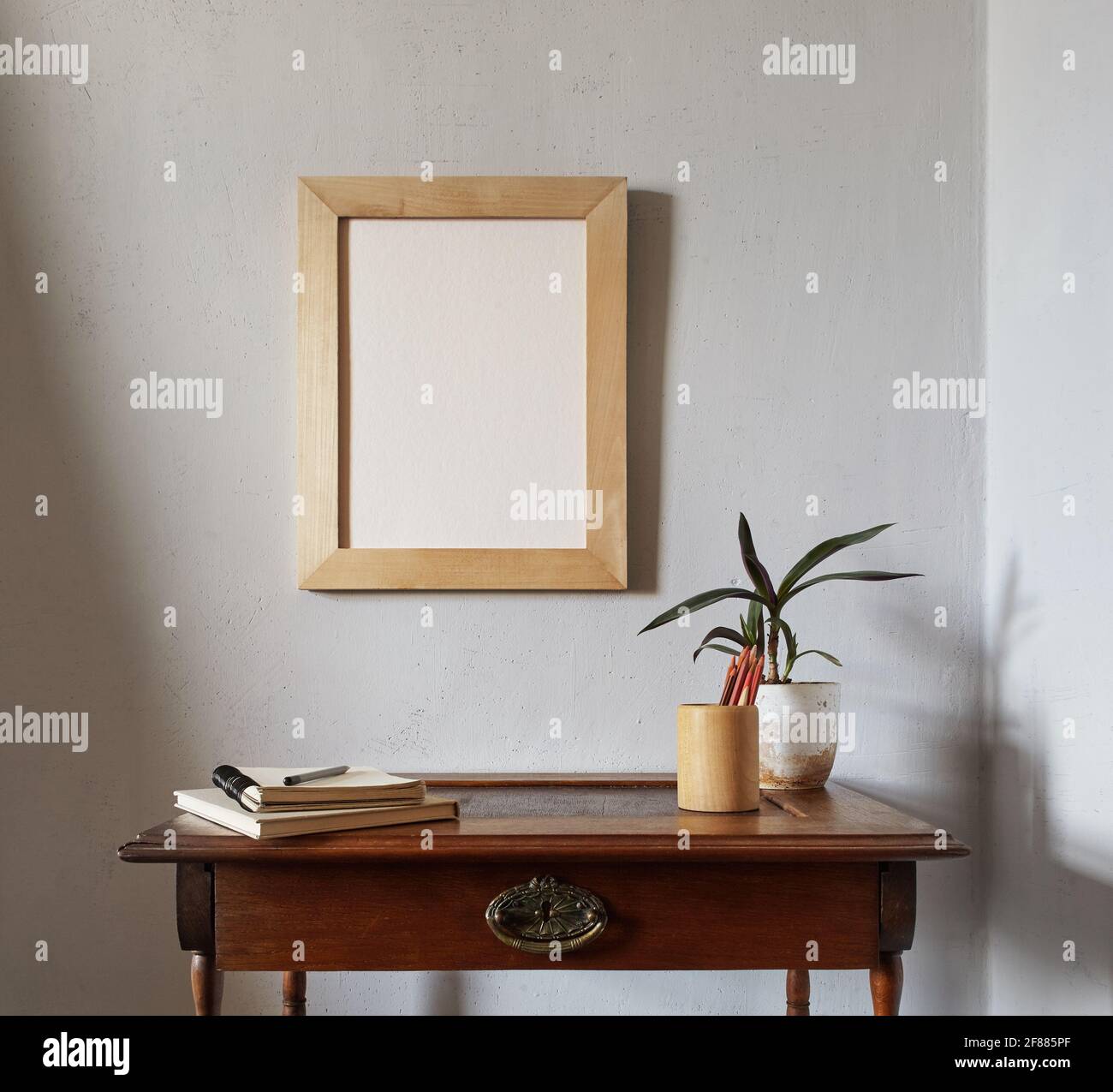 Modell mit Holzrahmen. Blumentopf auf einem Stapel Bücher auf einem alten Holzschreibtisch. Komposition auf weißem Wandhintergrund Stockfoto