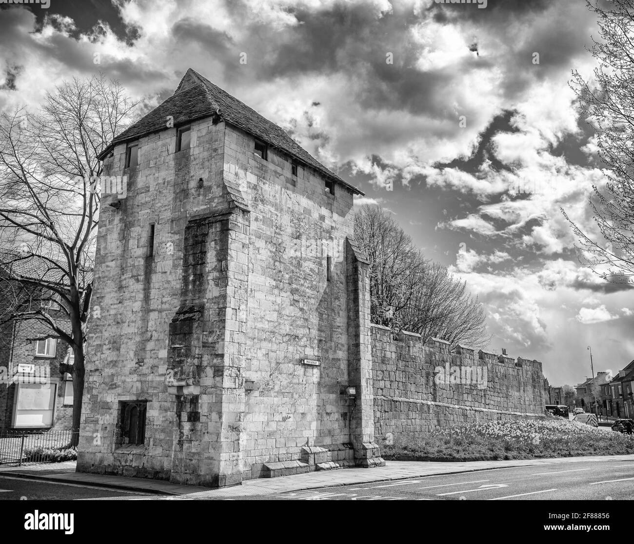 Ein hoher mittelalterlicher Turm am Ende einer Stadtmauer. Es gibt ein modernes Haus im Hintergrund und ein Himmel mit Wolken ist oben. Stockfoto