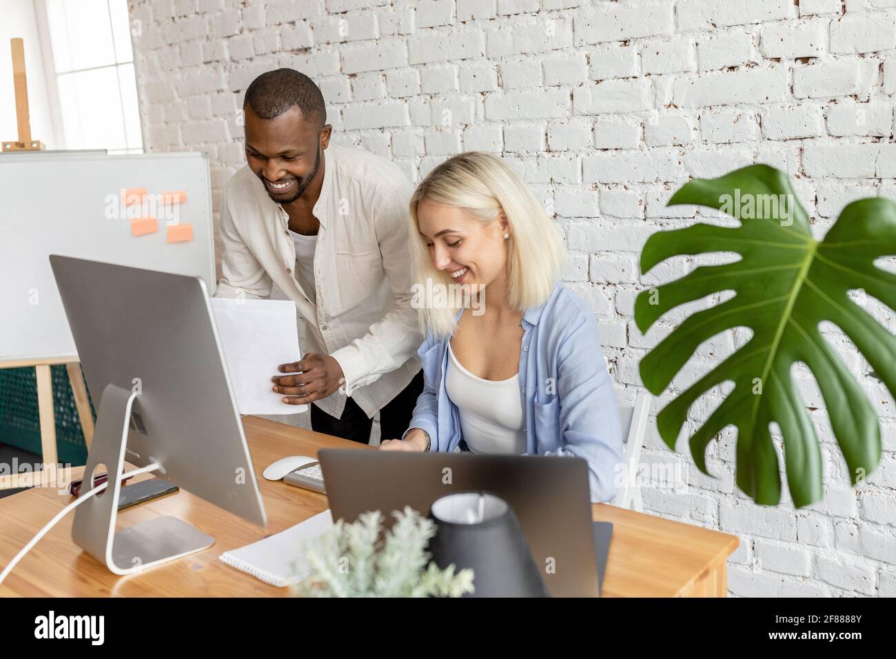 Fröhliche, multiethnische Mitarbeiter arbeiten in modernen Büros zusammen, lächeln und machen Papierkram. Glücklich erfolgreiche Kollegen diskutieren neues Projekt oder Stockfoto