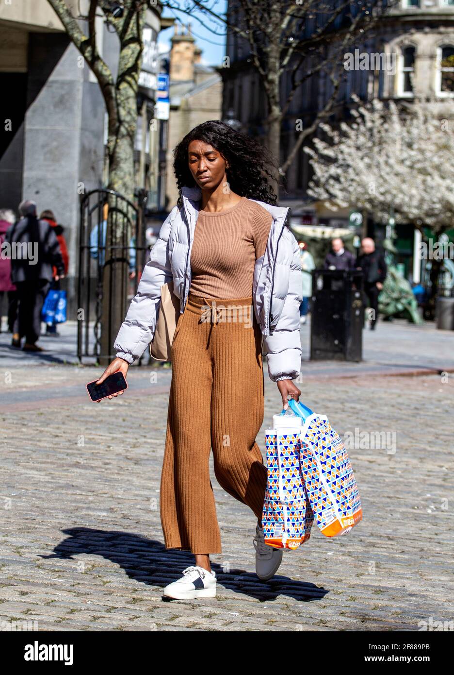 Dundee, Tayside, Schottland, Großbritannien. April 2021. UK Wetter: Ein sonniger Nachmittag mit einer leichten Kälte in der Luft über Nordostschottland mit Temperaturen von bis zu 9 Grad Die Sperrung von Covid-19 wird gelockert, da die Menschen weiterhin durch das Stadtzentrum schlendern und einige wichtige Einzelhandelsgeschäfte für Geschäfte geöffnet werden. Eine wunderschöne, große Afrikanerin aus Ghana nutzt die neuen Sperrbestimmungen und das sonnige Wetter, das nach einem langen Einkaufstag die Dundee High Street mit B&M-Plastiktragetaschen entlang führt. Kredit: Dundee Photographics/Alamy Live Nachrichten Stockfoto