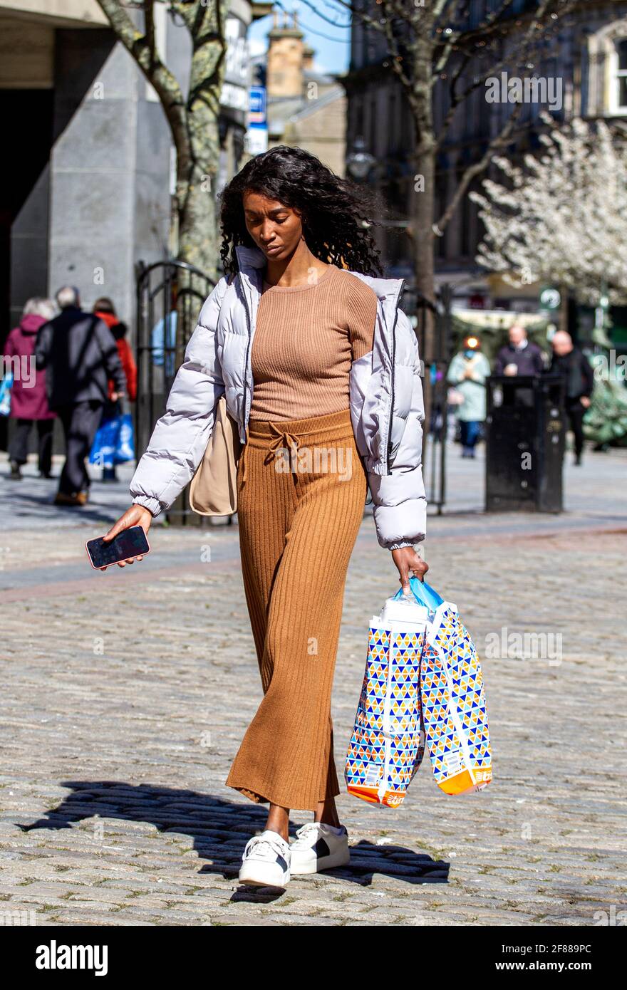 Dundee, Tayside, Schottland, Großbritannien. April 2021. UK Wetter: Ein sonniger Nachmittag mit einer leichten Kälte in der Luft über Nordostschottland mit Temperaturen von bis zu 9 Grad Die Sperrung von Covid-19 wird gelockert, da die Menschen weiterhin durch das Stadtzentrum schlendern und einige wichtige Einzelhandelsgeschäfte für Geschäfte geöffnet werden. Eine wunderschöne, große Afrikanerin aus Ghana nutzt die neuen Sperrbestimmungen und das sonnige Wetter, das nach einem langen Einkaufstag die Dundee High Street mit B&M-Plastiktragetaschen entlang führt. Kredit: Dundee Photographics/Alamy Live Nachrichten Stockfoto