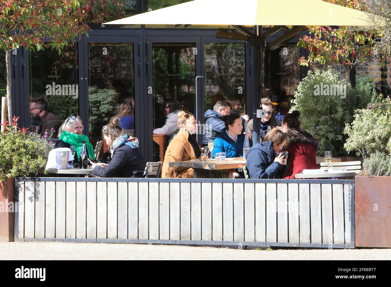 London, Großbritannien, 12. April 2021. Die Lighterman gasto Pub Terrasse am Regents Canal bei Kings Cross war voll, da das Essen im Freien wieder aufgenommen werden konnte, da die Sperre nachließ. Ein kalter Wind schreckt die Gäste nicht ab, die sich warm eingewickelt haben! Quelle: Monica Wells/Alamy Live News Stockfoto