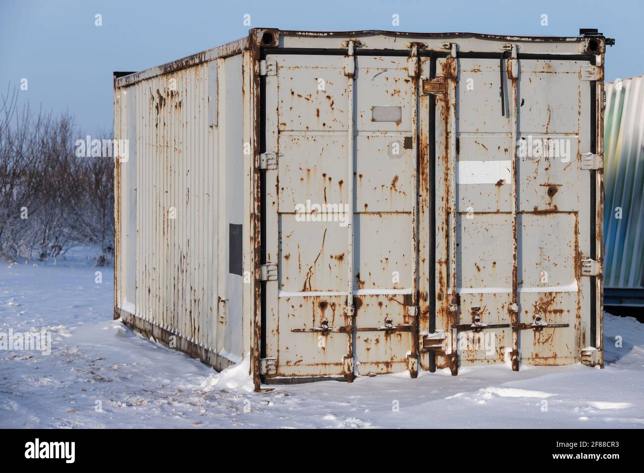 Rostiger grauer Frachtcontainer steht auf Schnee, industrielle Schifffahrtsausrüstung Stockfoto