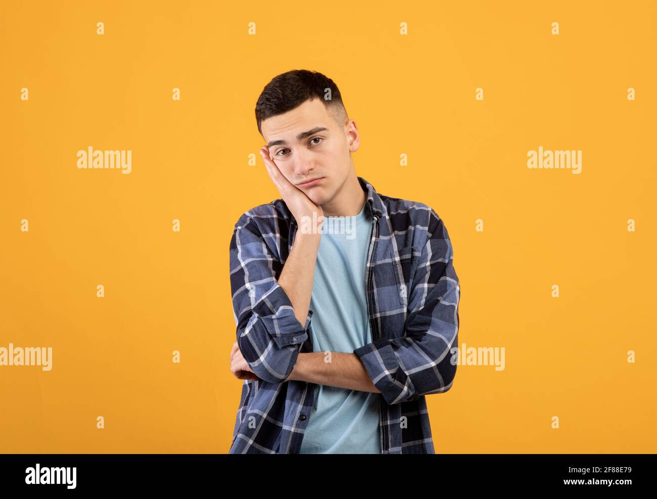 Porträt eines jungen Mannes, der sich gelangweilt fühlt, sich an seiner Hand lehnt und einen langweiligen Tag auf orangefarbenem Studiohintergrund hat Stockfoto