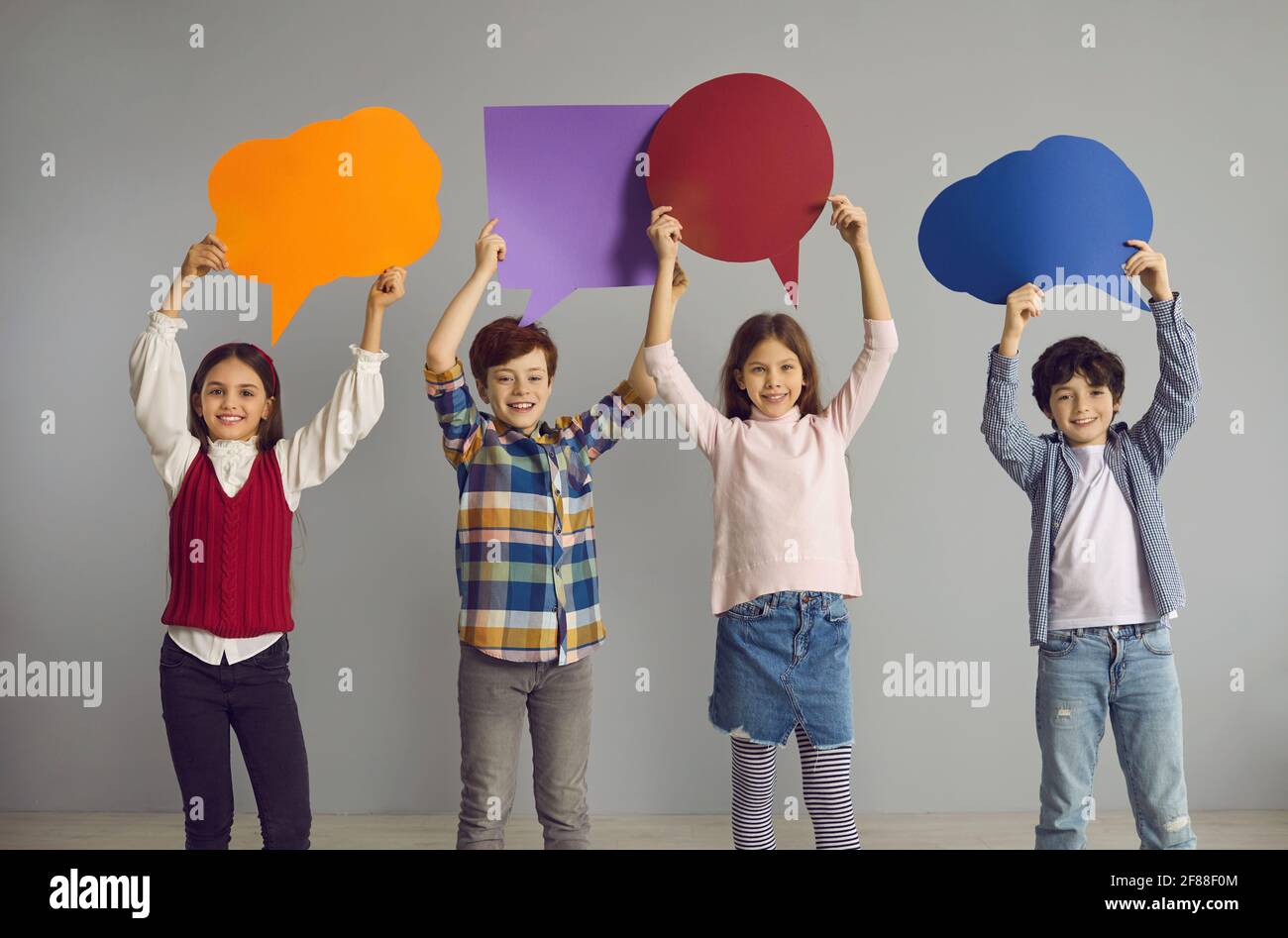 Eine Gruppe glücklicher Kinder, die im Studio stehen und farbenfroh zeigen Leere Sprechblasen Stockfoto
