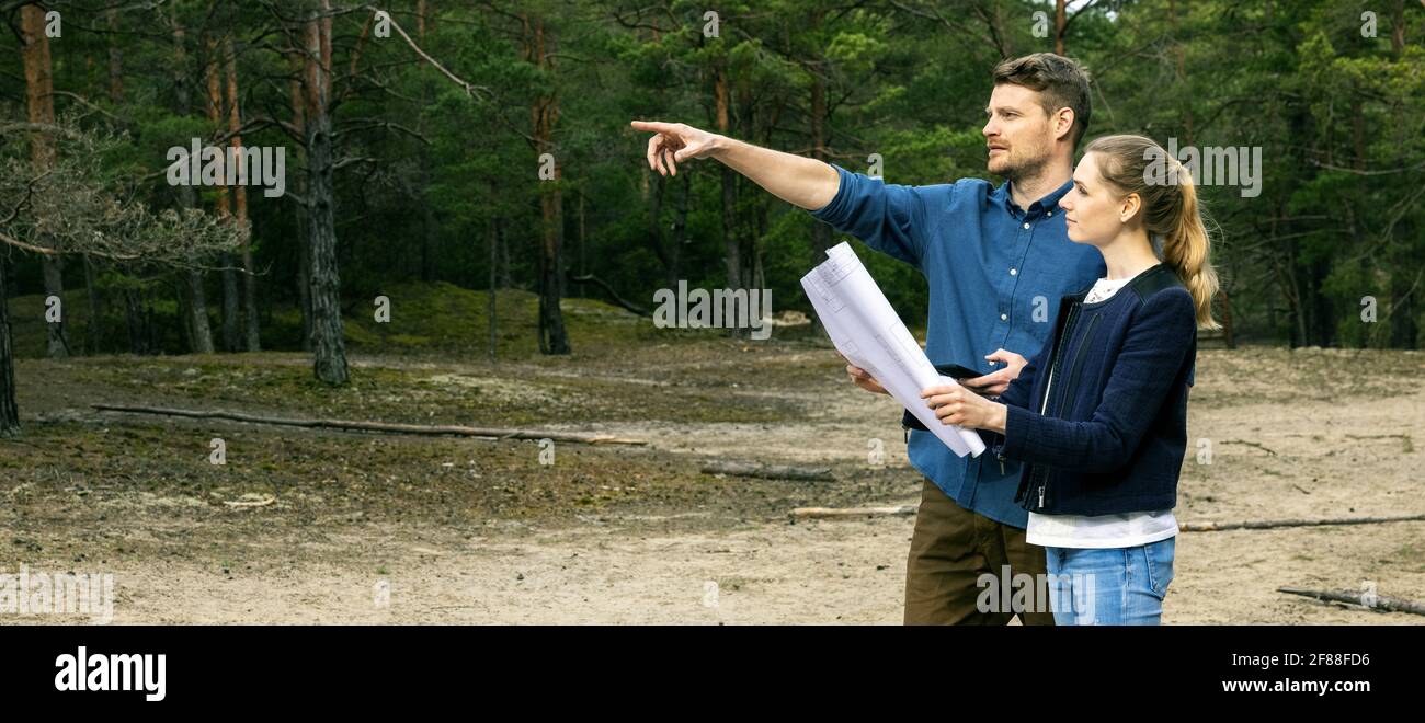 Junges Paar, das ein Grundstück für den Bau einer Waldhütte wählt. Banner-Kopierraum Stockfoto