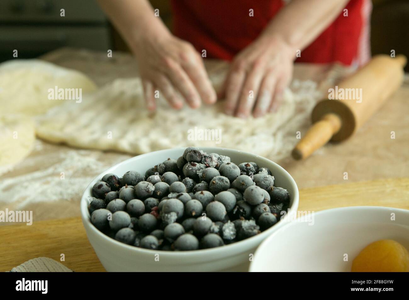 Mamas Kuchen. Füllung für Obstkuchen: Gefrorene schwarze Johannisbeere. Vor dem Hintergrund der Hände meiner Mutter bereiten sie den Teig für den Kuchen vor. Garzeit Stockfoto