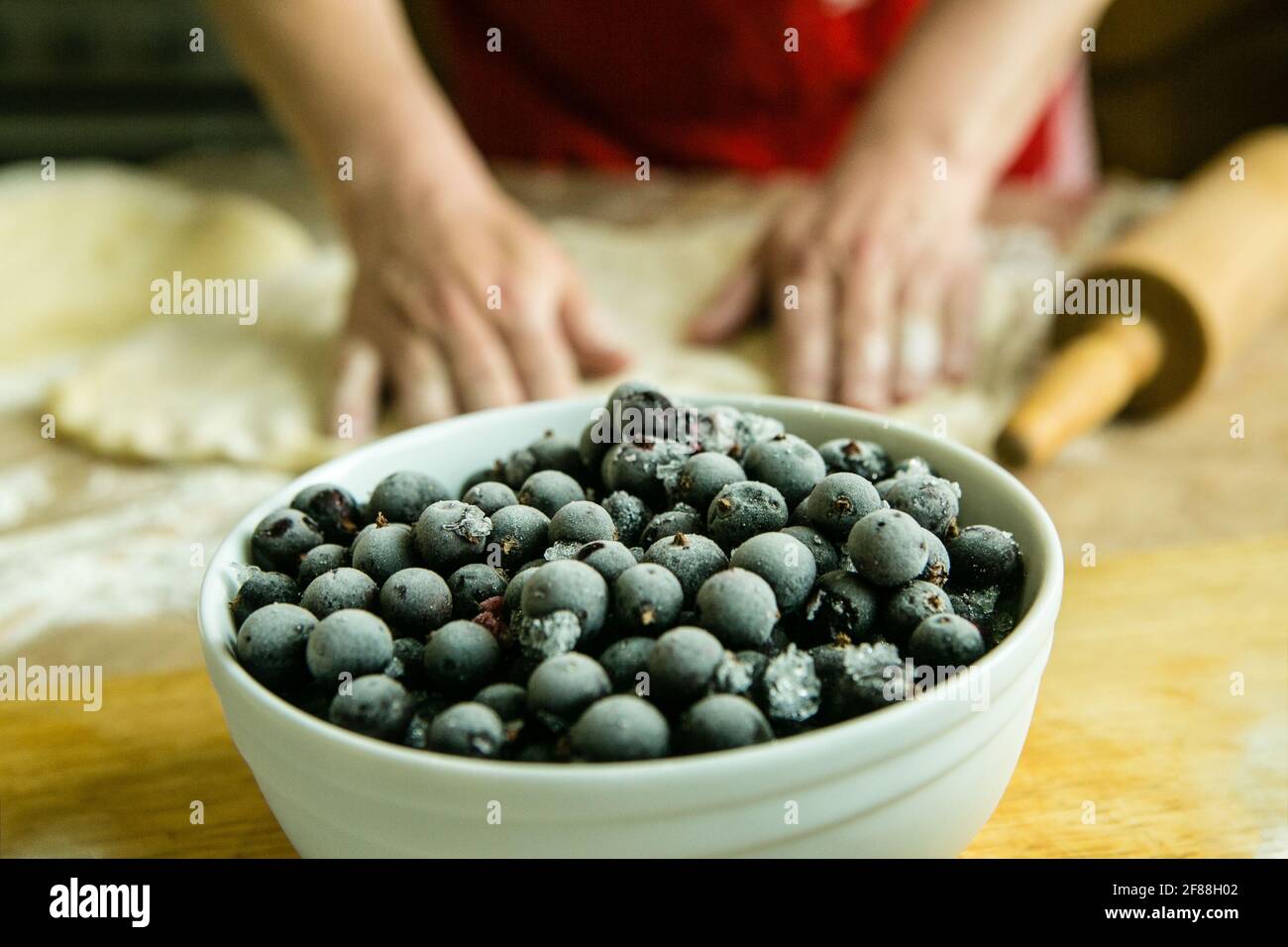Mamas Kuchen. Füllung für Obstkuchen: Gefrorene schwarze Johannisbeere. Vor dem Hintergrund der Hände meiner Mutter bereiten sie den Teig für den Kuchen vor. Garzeit Stockfoto