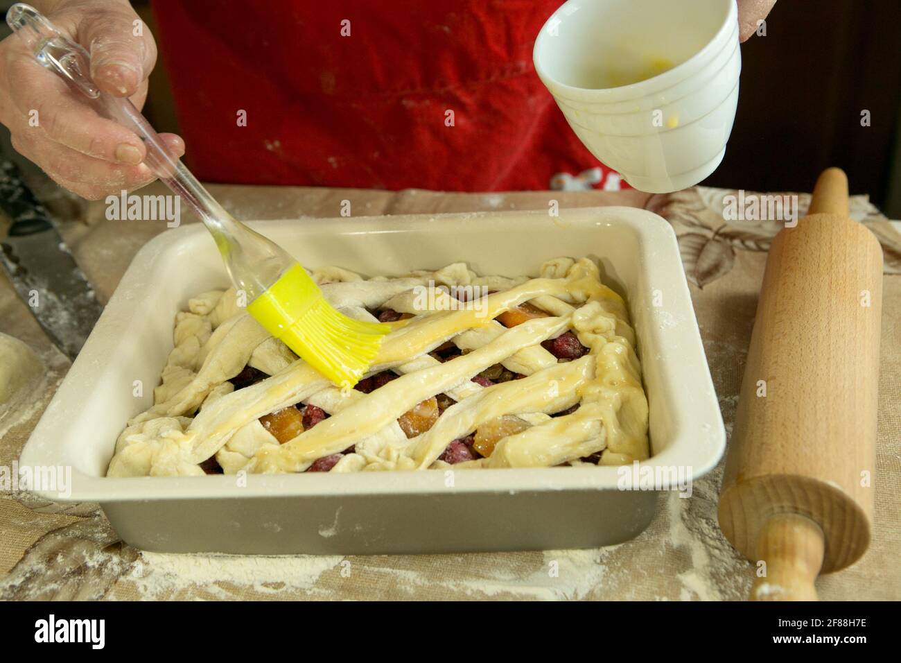 Mamas Kuchen. MUM schmiert den Kuchen vor dem Backen mit einer Kochbürste. Weibliche Hände. Kochen während der Quarantäne. Stockfoto