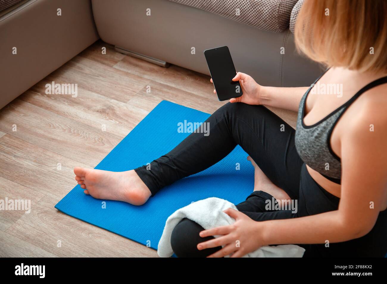 Mockup für App Online-Fitness-Programm, Remote Yoga-Klasse. Frau in Sportbekleidung hält Smartphone mit leerem Bildschirm für Sport oder Musik-App während eines Wor Stockfoto
