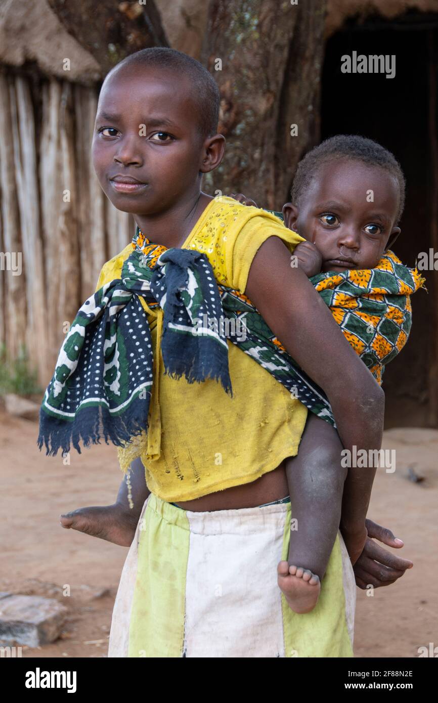 Das junge Maasai-Mädchen mit einem Baby, das an ihren Rücken gebunden ist Stockfoto