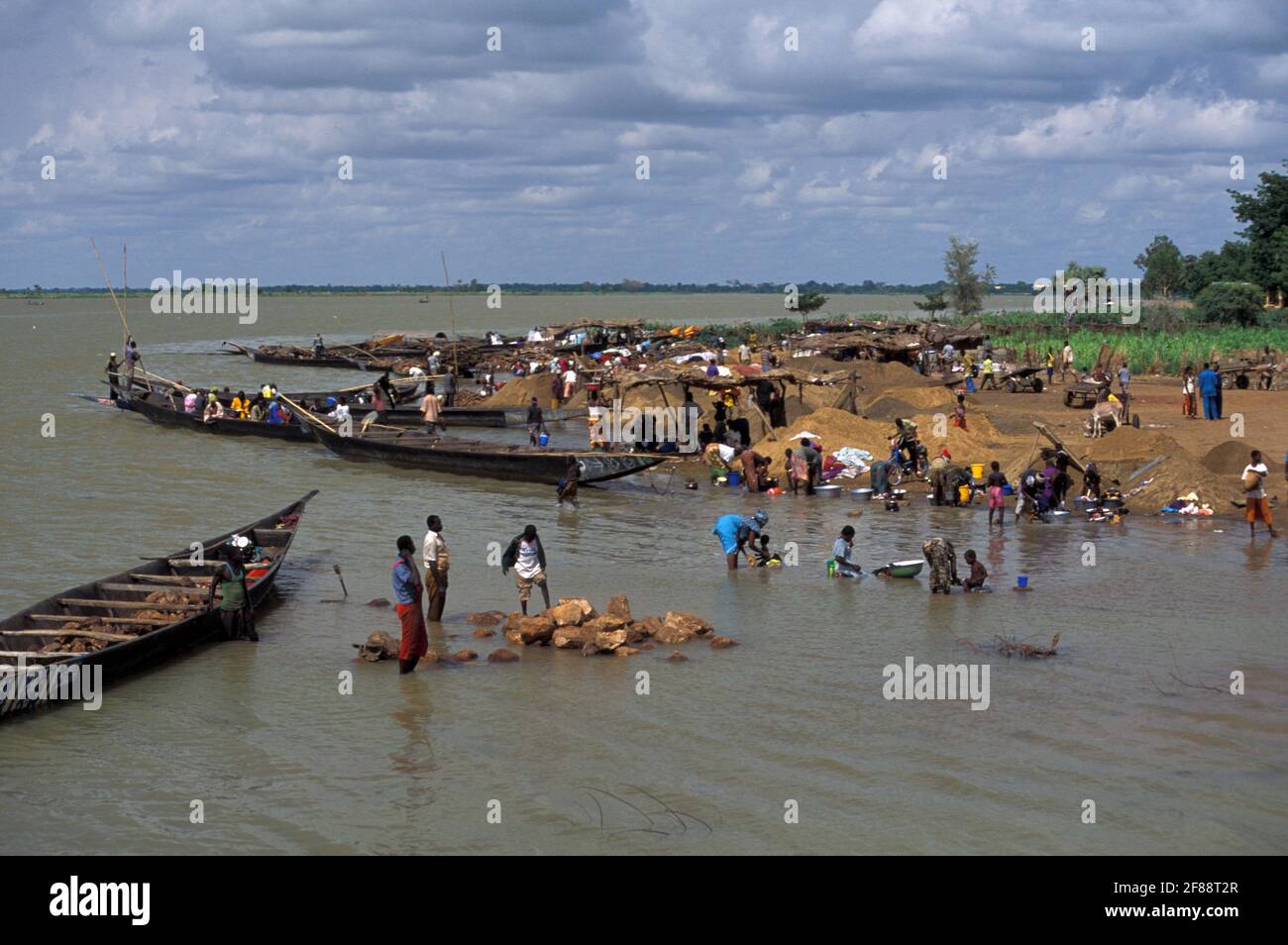 Dorf mit Frauen, die am Ufer des Niger waschen, und Männern, die Steine in Pirogue, Ségou, Mali transportieren Stockfoto