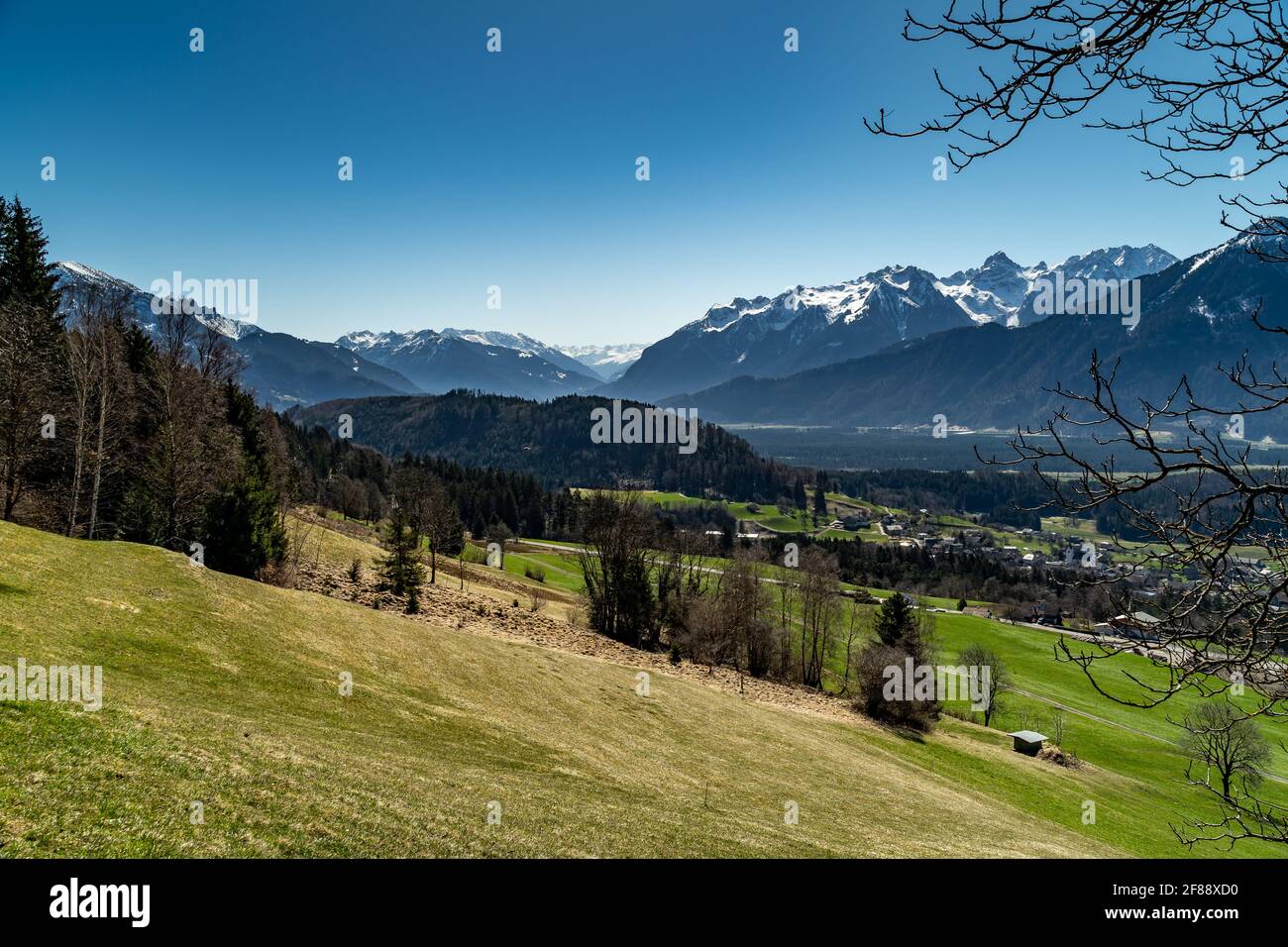 Walgau mit Schlins und den Bergen von Arlberg bis Rhätikon und Zimba. Sonniger Frühlingstag mit wolkenlosem Himmel, Bäumen, verschneiten Bergen Stockfoto