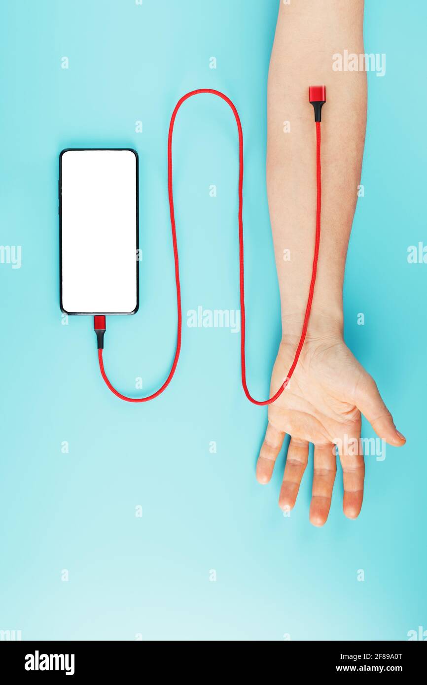 Die Hand wird über ein rotes Netzkabel mit einem Smartphone mit freiem Speicherplatz auf blauem Hintergrund verbunden. Das Konzept der Drogenabhängigkeit in den sozialen Netzwerken o Stockfoto