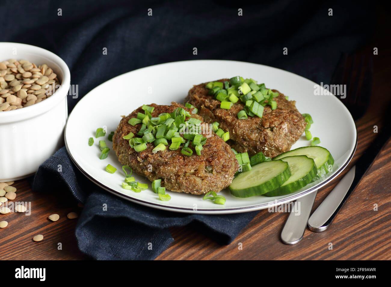 Linsenschnitzel garniert mit grünen Zwiebeln und Gurke auf rustikalem Holztisch, Nahaufnahme, vegetarisches fastenöstgericht, gesundes veganes Lebensmittelkonzept Stockfoto