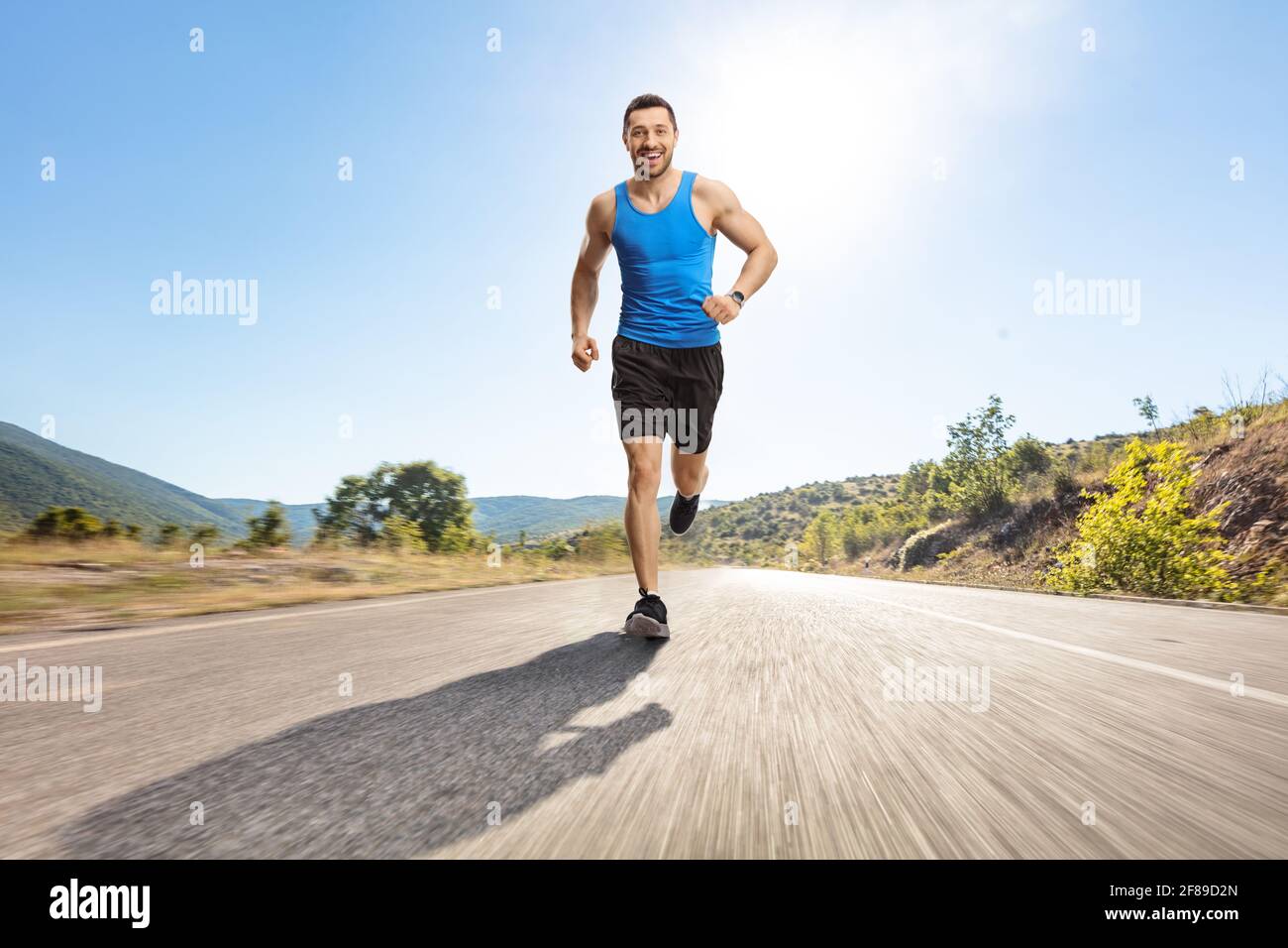 Ganzkörperportrait eines jungen Mannes, der auf einem joggt Asphaltierte Straße zur Kamera Stockfoto
