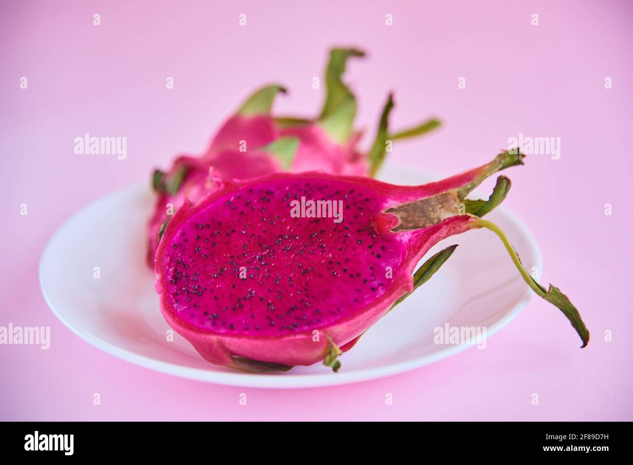 Teller mit tropischen exotischen Drachenfrucht-Pitaya. Ernährung reife rohe asiatische Früchte köstlich. Pitahaya in 2 Hälften auf rosa Hintergrund geschnitten Stockfoto