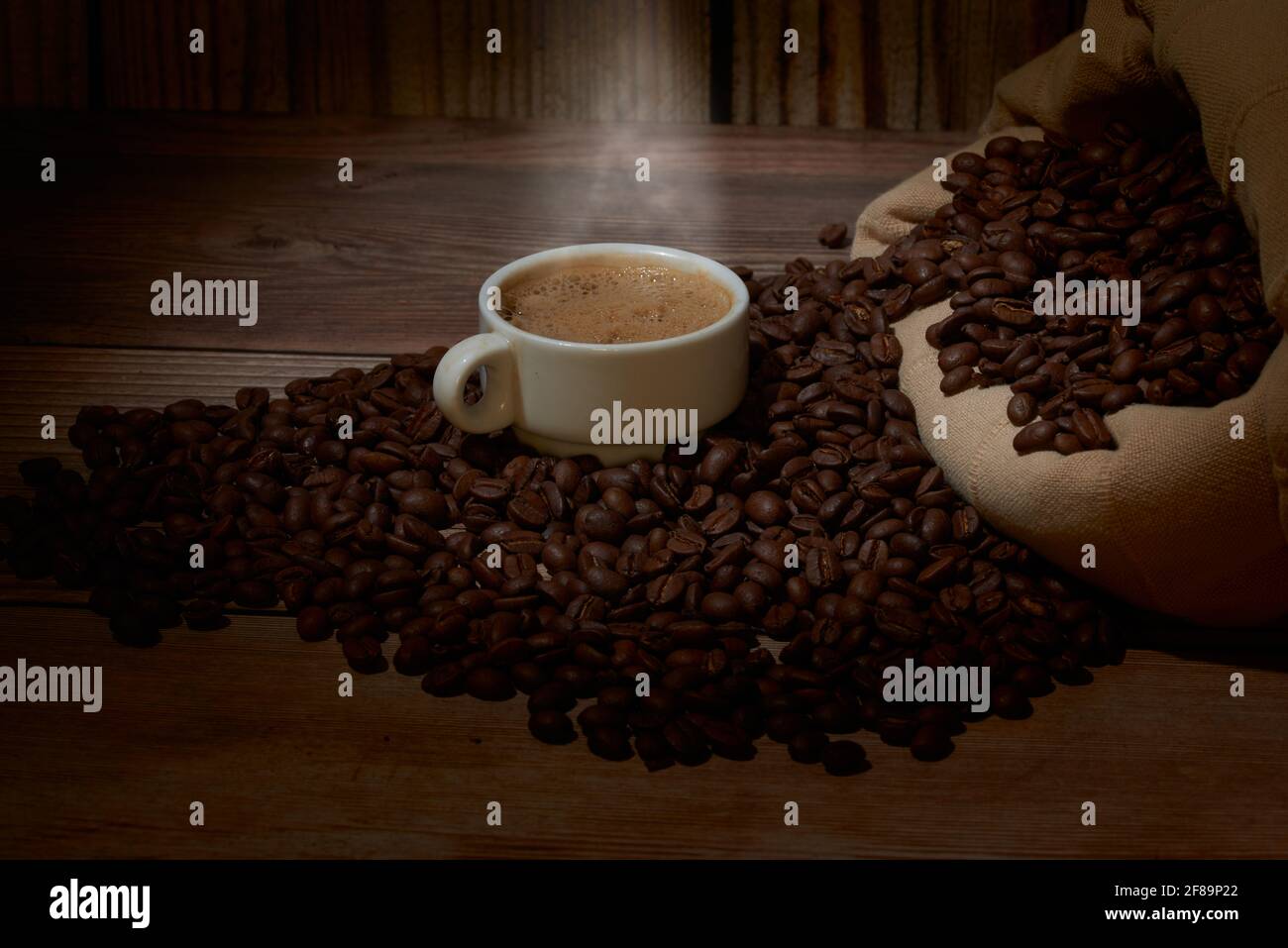 Ein leckerer Kaffee auf einem Holzbrett, umgeben von Bohnen Stockfoto