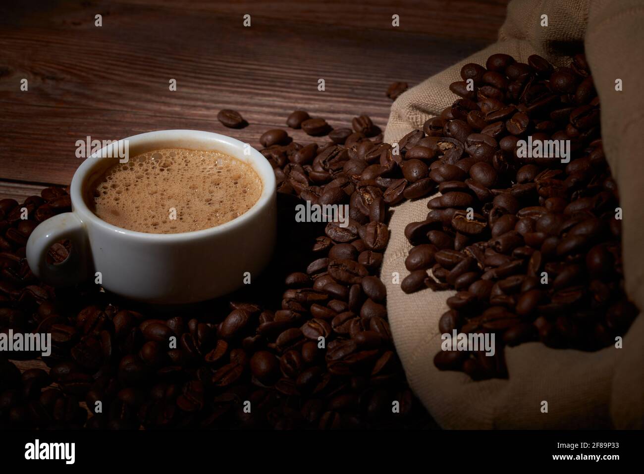 Ein leckerer Kaffee auf einem Holzbrett, umgeben von Bohnen Stockfoto