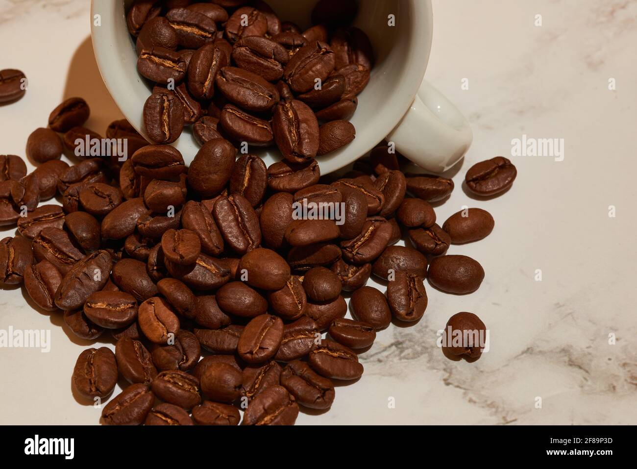 Einige reiche Kaffeebohnen, die aus einer liegenden Tasse kommen Auf seiner Seite Stockfoto