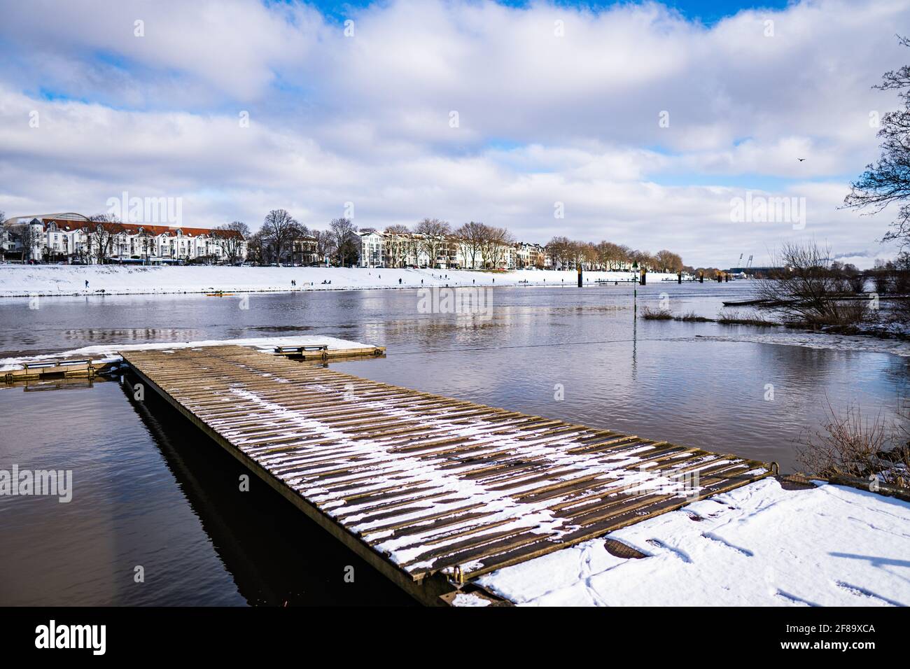 Blick über die weser, den verschneiten osterdeich und die hölzerne Landestelle im Winter in bremen mit Stadion im Hintergrund Stockfoto