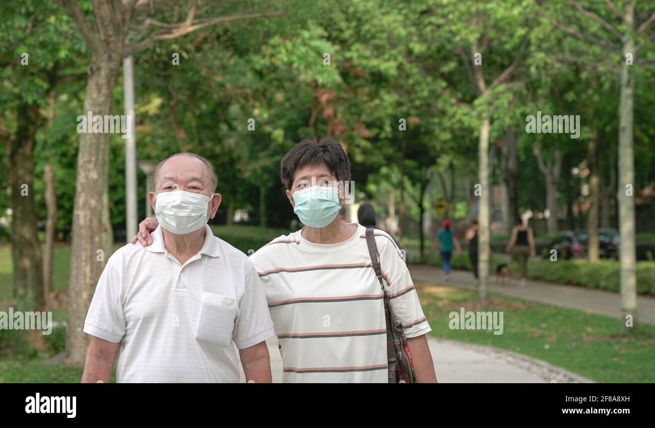 Ein erfahrenes asiatisches Paar mit Gesichtsmaske, das in einem grünen Park spazieren geht. Stockfoto