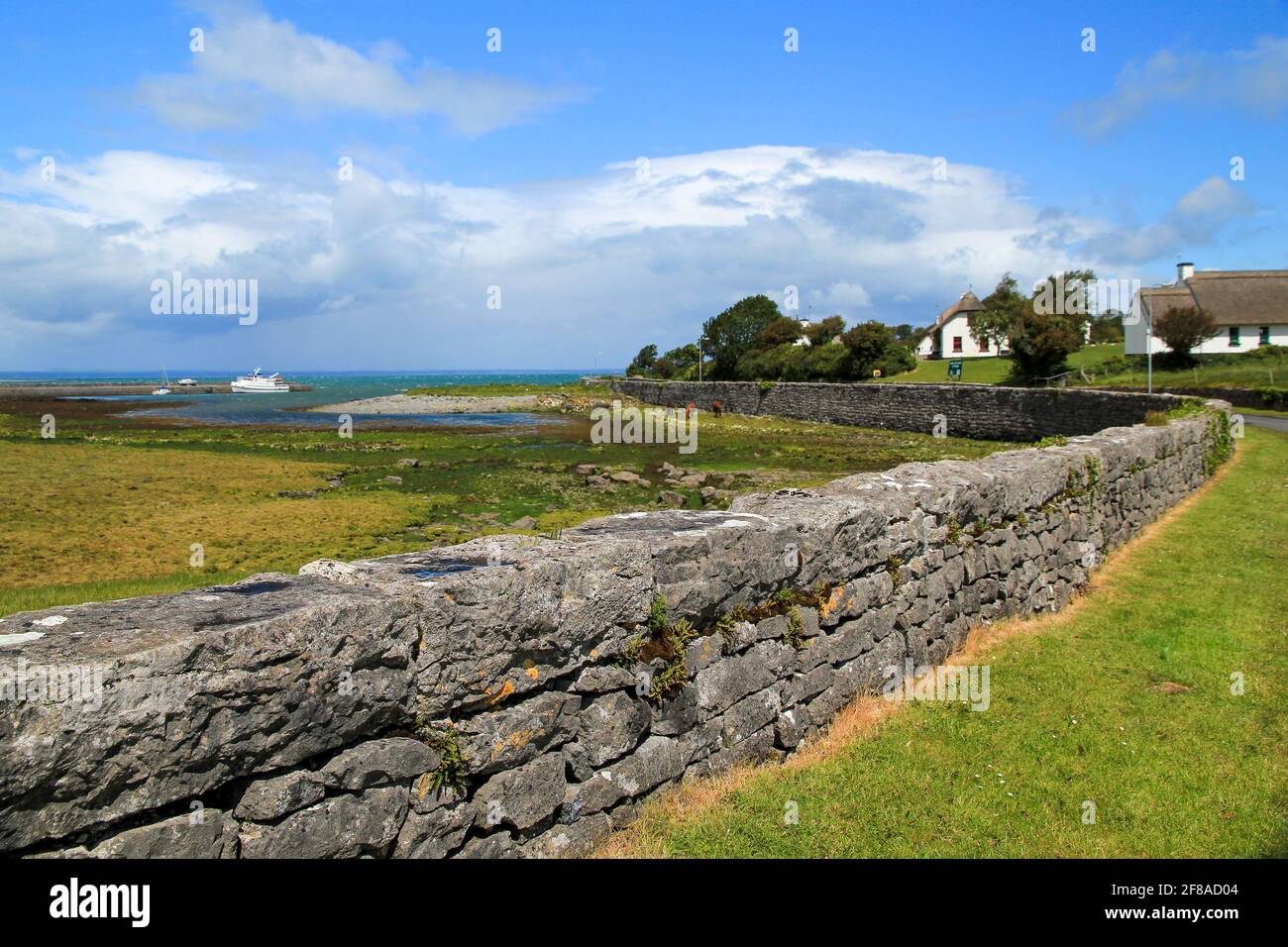 Curving Stone Fence entlang des Hafens bei Low Tide mit Grün Gras und blauer Himmel in der Grafschaft Clare Irland Stockfoto