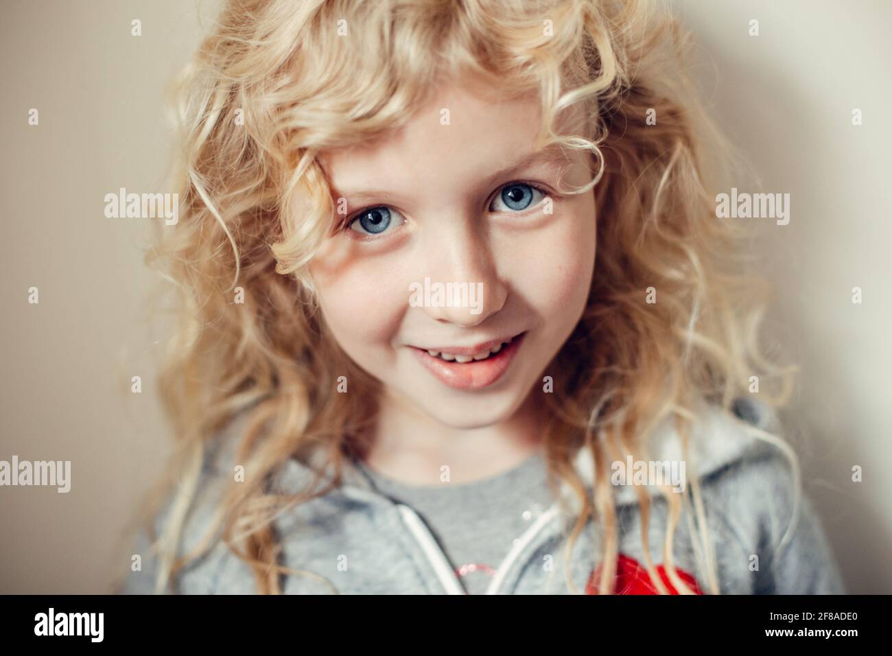 Nahaufnahme Porträt von schönen lächelnden kaukasischen blonden Mädchen mit langen Haaren auf hellem neutralen beigen Hintergrund. Ziemlich echtes Mädchen Kind Stockfoto