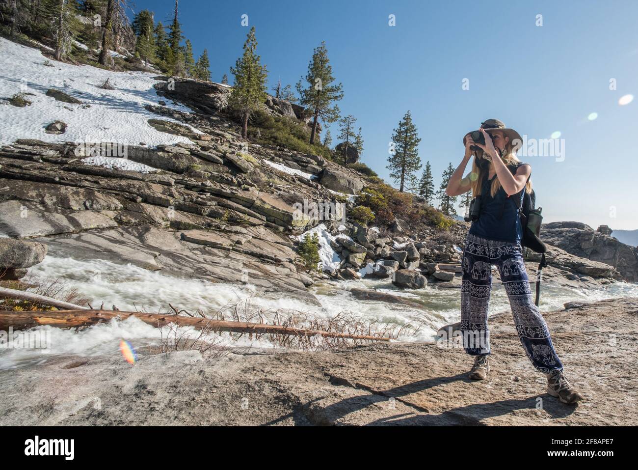 Eine Fotografin nimmt sich einen Moment Zeit, um ein Foto entlang eines malerischen Flusses und der Berge im Yosemite National Park, Kalifornien, zu machen. Stockfoto
