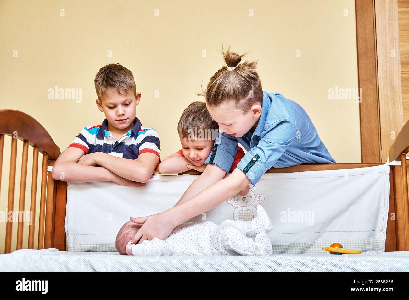 Glückliche ältere Brüder schauen sorgfältig und berühren sanft liebliches Baby Geschwister tragen weichen weißen Körper und liegen in Holzkrippe Stockfoto