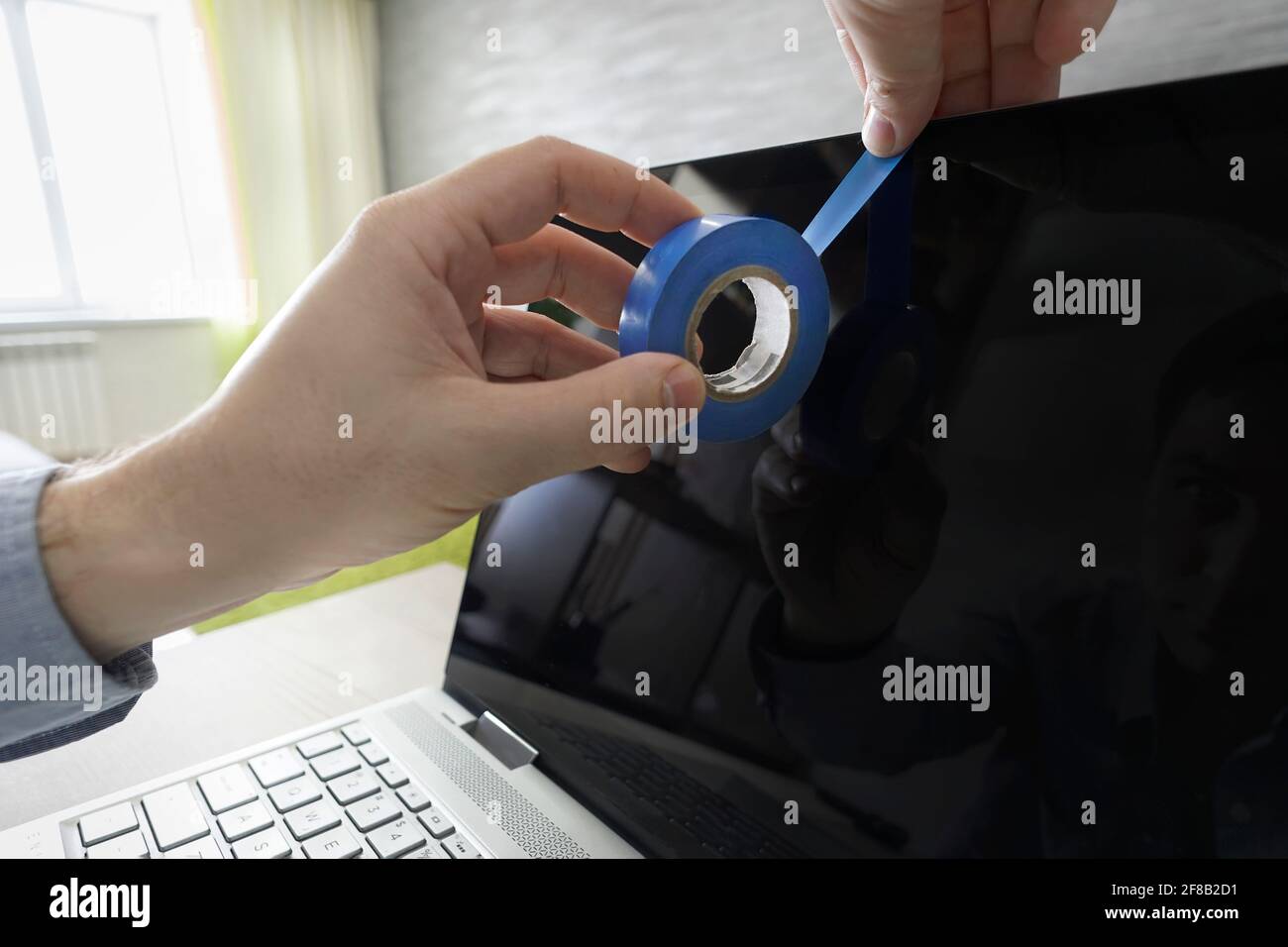 Menschliche Hand blockiert eine Webcam mit Laptop durch ein Klebeband. Verfolgungswahn, Verfolgungskomplex, Verblendung der Verfolgung. Ausspionieren von Privatsphäre über Webca Stockfoto