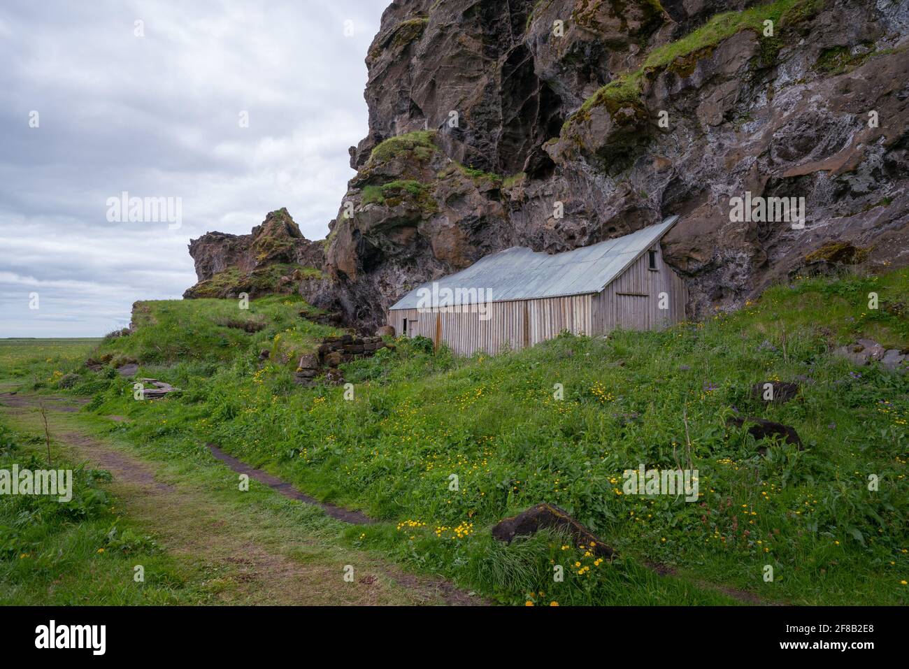 Haus in vulkanischem Gestein im Süden Islands gebaut. Wolkiger Tag, Gras im Vordergrund. Stockfoto