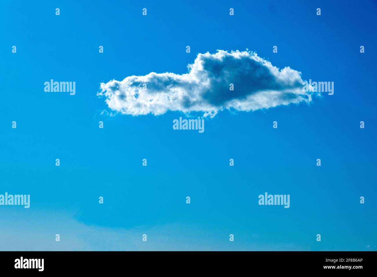 Einzelne weiße Wolke isoliert gegen tiefblauen Himmel Stockfoto