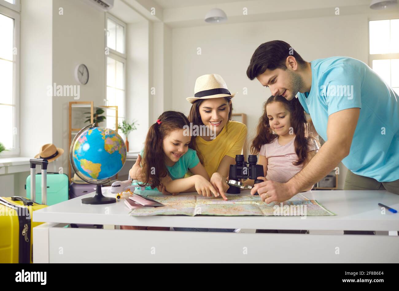 Fröhliche und aktive Eltern mit lächelnden Kindern schauen sich die Karte an und entscheiden, wohin sie in den Urlaub fahren sollen. Stockfoto