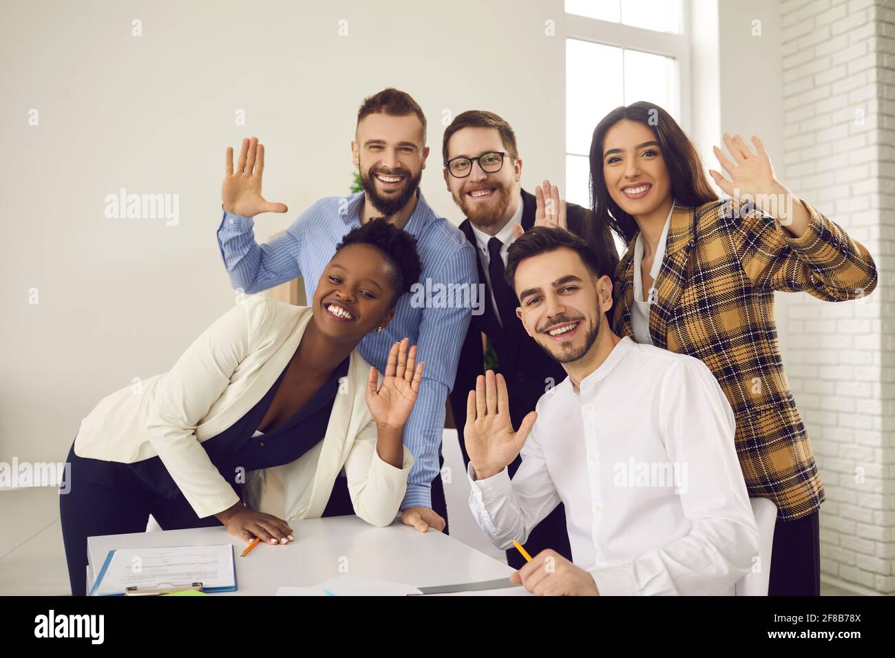 Gruppenportrait von glücklichen jungen Geschäftsleuten, die mit den Händen zuwinken Kamera und Lächeln Stockfoto