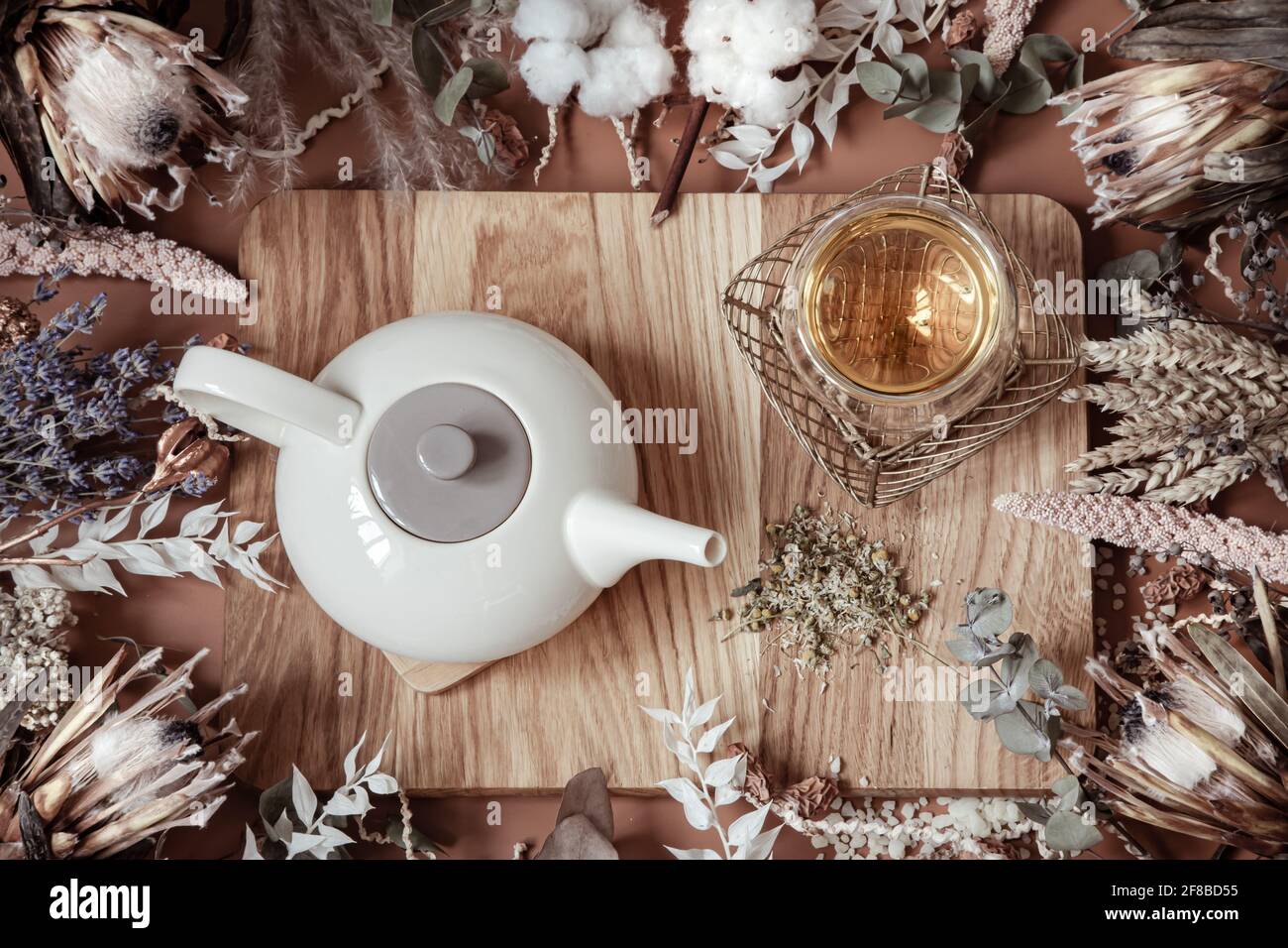 Komposition mit trockenen Wildblumen und natürlichem Kräutertee in einer Teekannen auf einer Holzoberfläche. Stockfoto