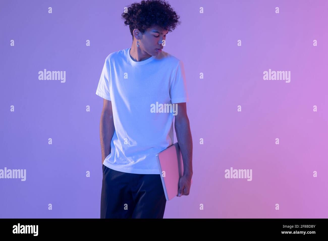 Lockiger junger Mann in weißem T-Shirt mit einem Laptop Stockfoto