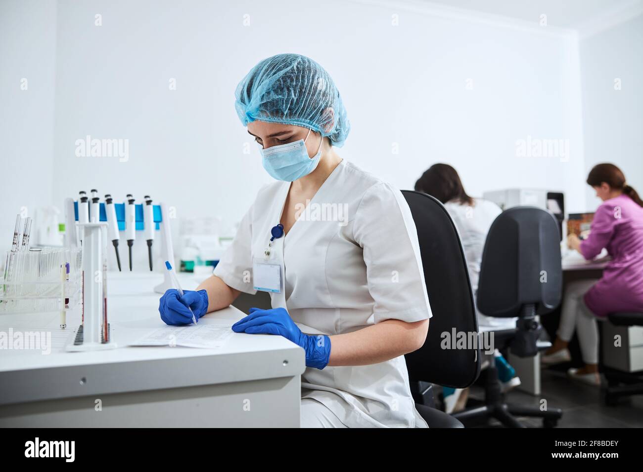 Eine Biochemikerin in einer Gesichtsmaske, die ein Wissenschaftslabor schreibt Bericht Stockfoto