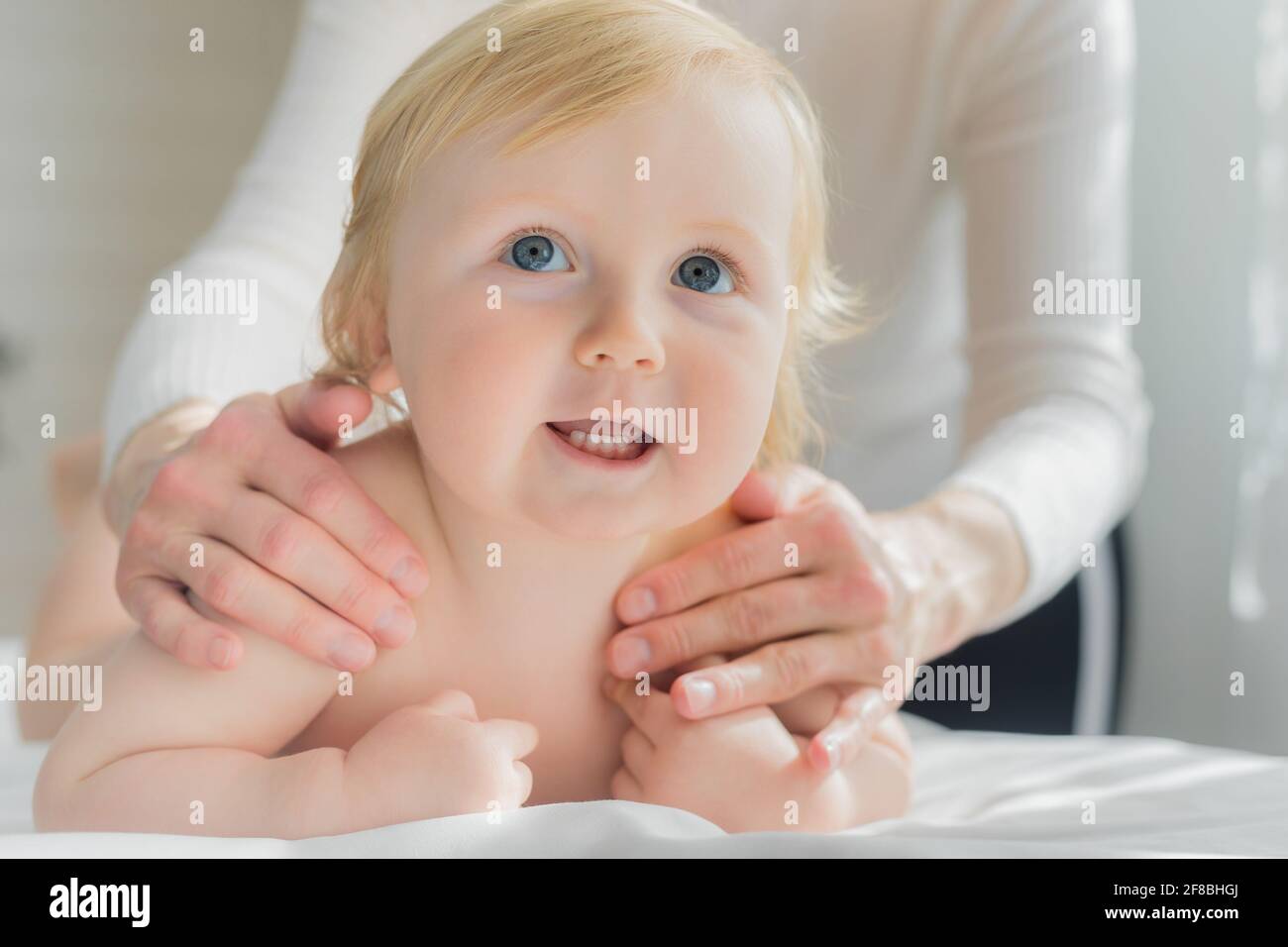 Mama gibt ihrem Baby eine Schulter- und Rückenmassage. Nahaufnahme. Ein zufriedenes Baby liegt auf dem Massagetisch. Stockfoto