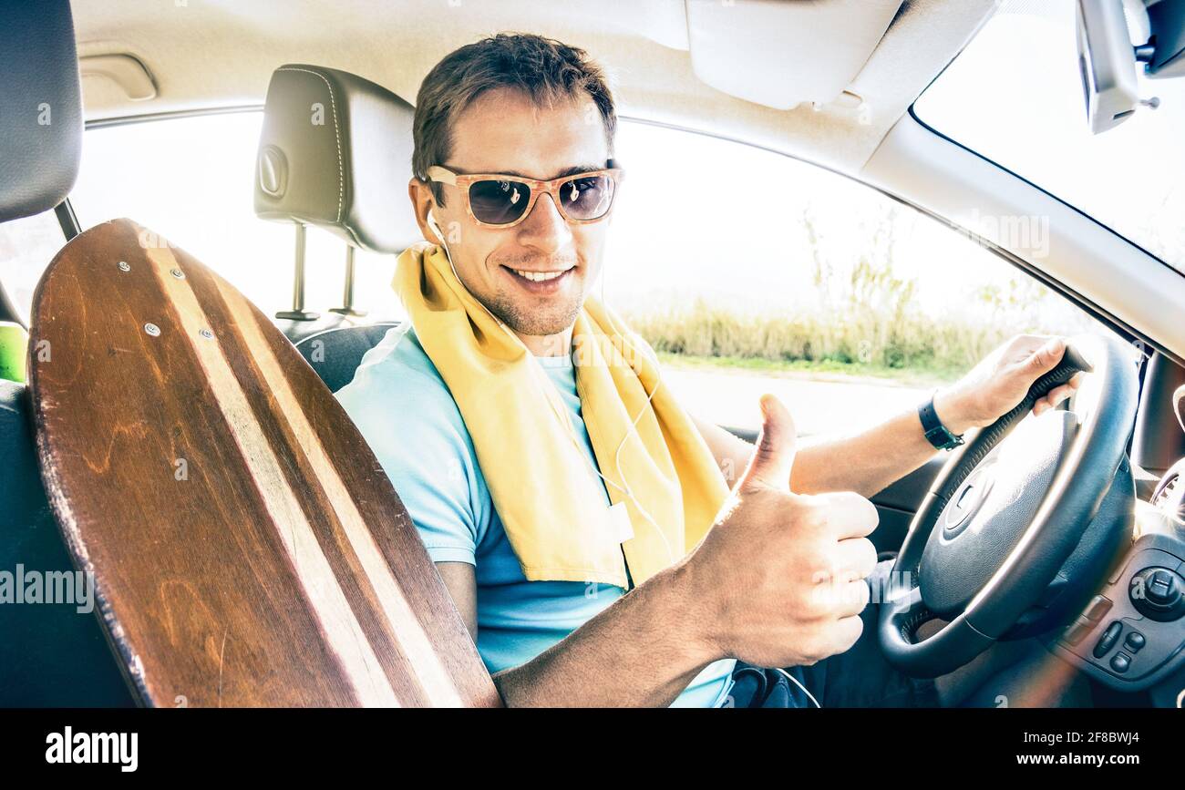 Junge Hipster-Modelmann, der Auto mit Longboard fährt Frühlingsferien Sommerstimmung - glücklicher selbstbewusster Mann mit Daumen Lächelnd auf die Kamera schauen Stockfoto