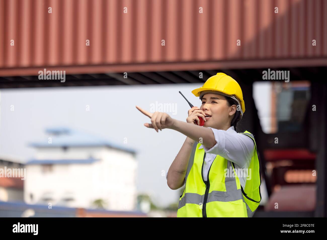 Fabrikarbeiterin oder Ingenieurin mit Walkie-Talkie und Telefonieren Jemand für die Vorbereitung eines Jobs im Lagerhaus der Behälter Stockfoto