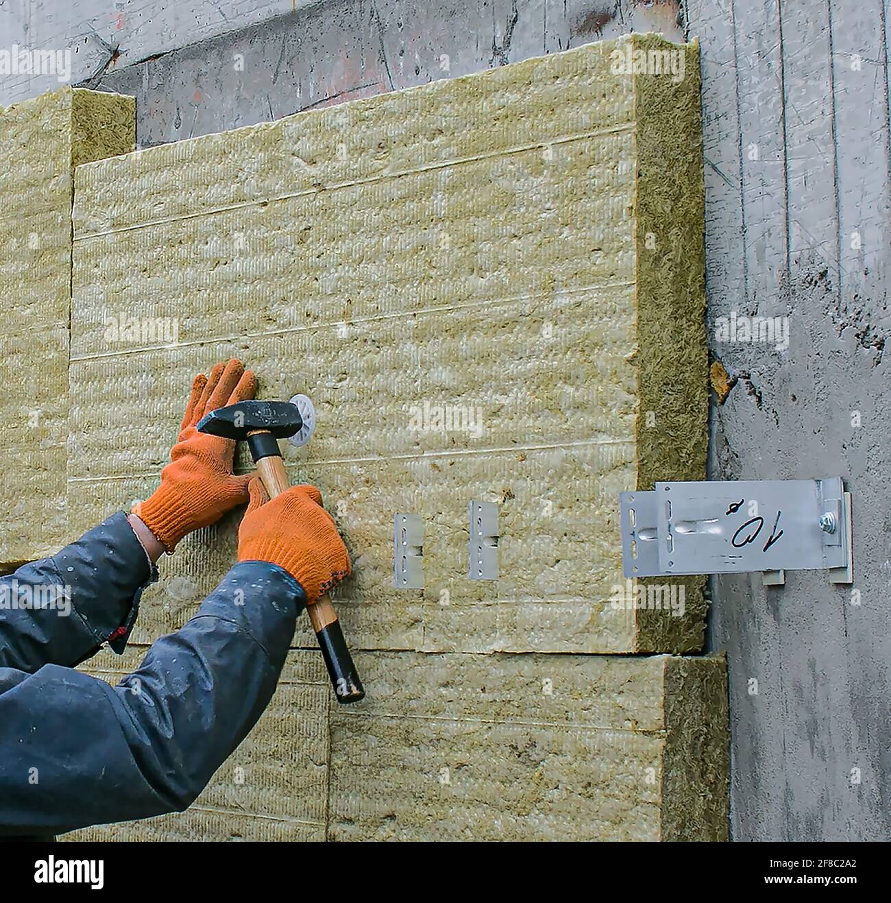 Ein Mann installiert eine Schicht Wärmedämmung an der Wand der Treppe draußen - mit Mineralwollplatten. Das Konzept der Reparatur und Isolierung von ex Stockfoto