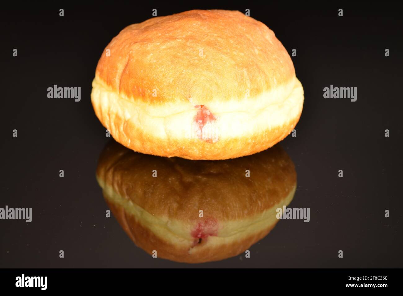 Ein frisch gebackener appetitlich, schmackhafter, süßer Donut mit Kirschfüllung, Nahaufnahme, auf schwarzem Hintergrund. Stockfoto