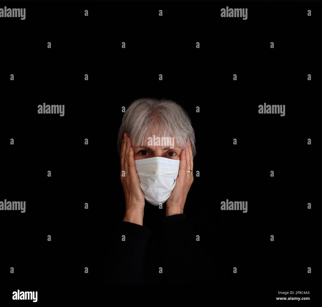 Ältere Frau mit Kopfschuss, Gesichtsmaske mit Coronavirus, Kopf in den Händen. Verzweiflung, Stress-Konzept auf schwarzem Hintergrund. Stockfoto
